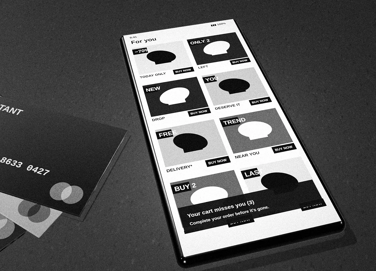 Black-and-white photograph of a smartphone lying on a table showing a shopping feed titled For you, with BUY NOW buttons and a notification: Your cart misses you.